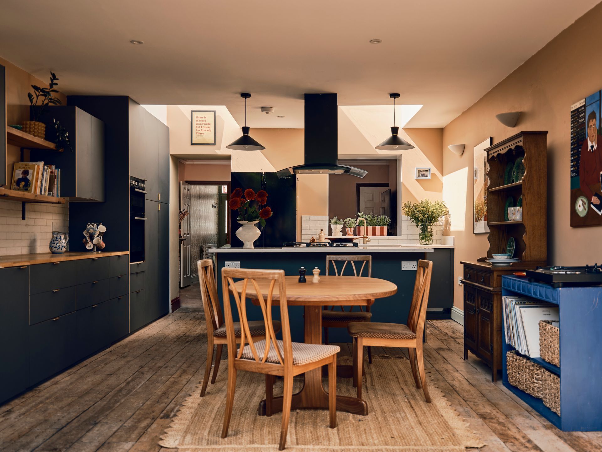 Open-plan kitchen designed by Heather Brazier with navy cabinetry, a round mid-century dining table and warm plaster-pink walls
